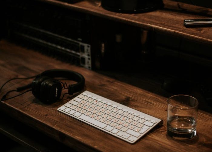 A cozy recording studio setup featuring a keyboard, headphones, and monitor on a wooden desk.